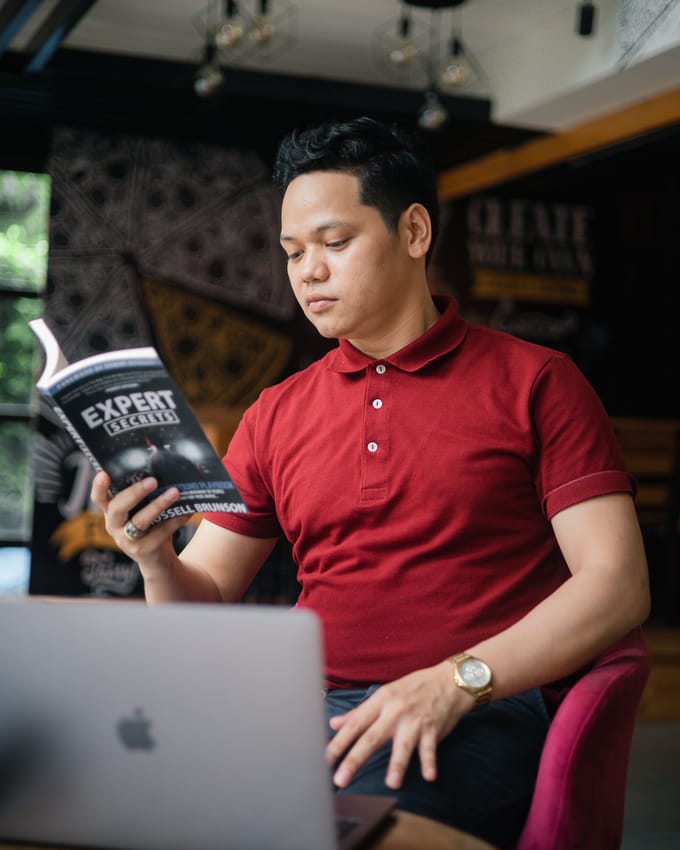 Jayvee Respeto, founder of AZ Digital PH, seated at a laptop and reading a book, wearing a red polo shirt